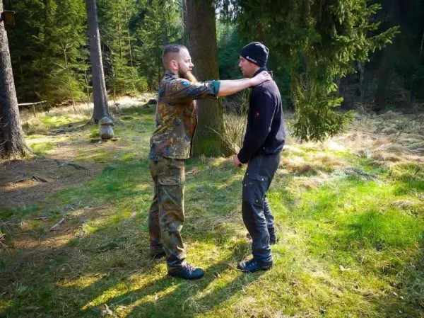 Person zeigt einer anderen Person eine Technik im Wald
