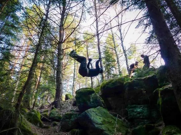Selbstgebaute Seilquerung über Felsen im Wald, eine Person hängt daran