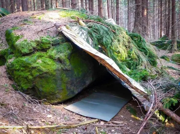 Tarp-Notunterkunft unter einem großen, moosbedeckten Felsen im Wald