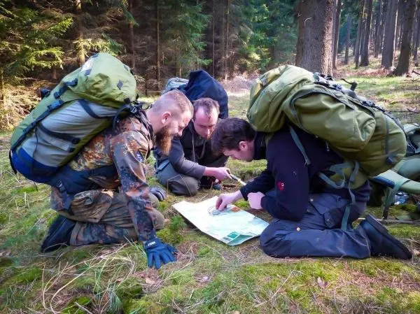 Vier Personen mit Rucksäcken studieren eine Karte im Wald