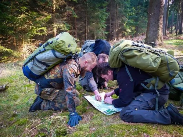 Vier Personen mit Rucksäcken studieren eine Karte im Wald