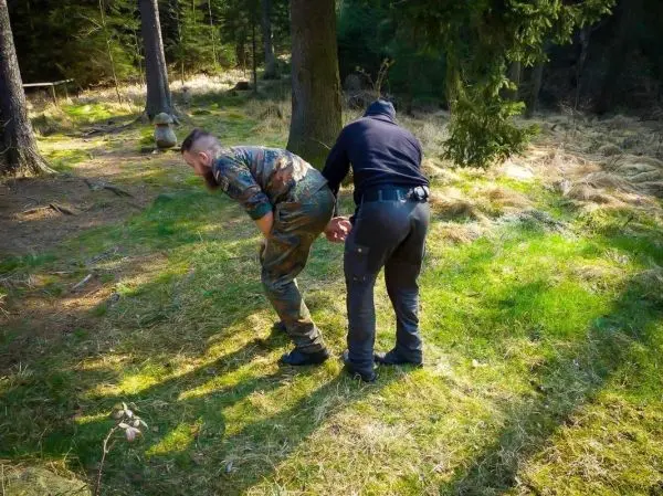 Zwei Personen in Tarnkleidung und schwarzer Kleidung führen eine Festnahme im Wald durch