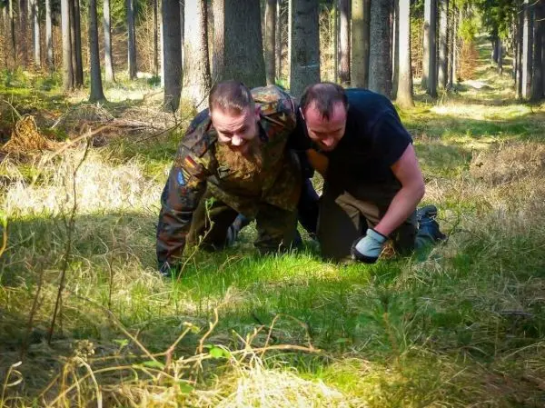 Zwei Personen kriechen auf dem Boden durch einen Wald mit hohem Gras