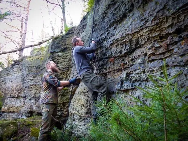 Zwei Personen nutzen ein Seil, um eine steile Felswand zu erklimmen