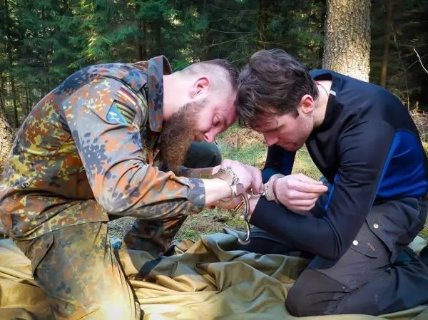 Zwei Personen sitzen auf einer Plane und legen Handschellen an