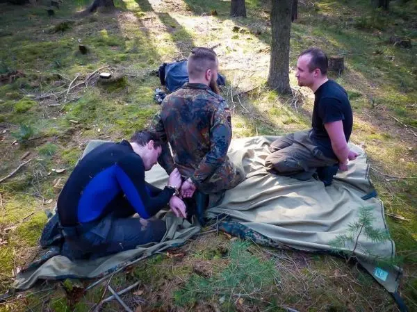 Zwei Personen sitzen auf einer Tarp-Notunterkunft, eine wird gefesselt