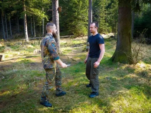 Zwei Personen stehen in einem Waldgebiet und sprechen miteinander