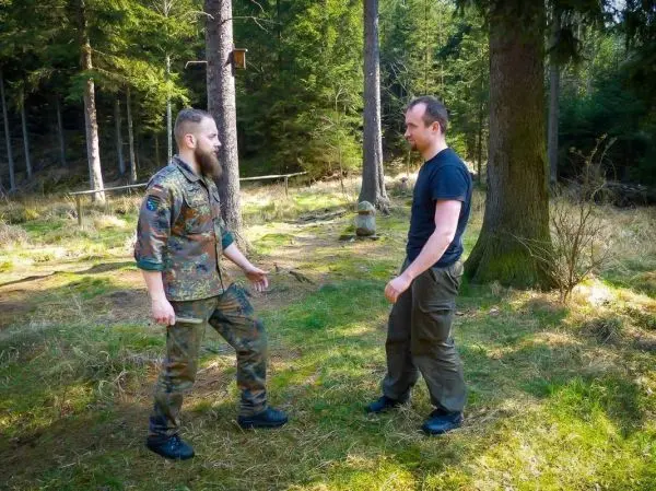 Zwei Personen stehen sich in einem Waldgebiet gegenüber und scheinen zu kommunizieren