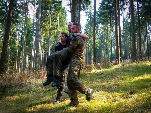 Zwei Personen tragen einen dritten Mann durch einen Wald