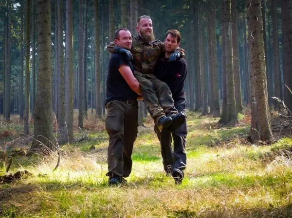 Zwei Personen tragen einen Mann durch einen Waldweg