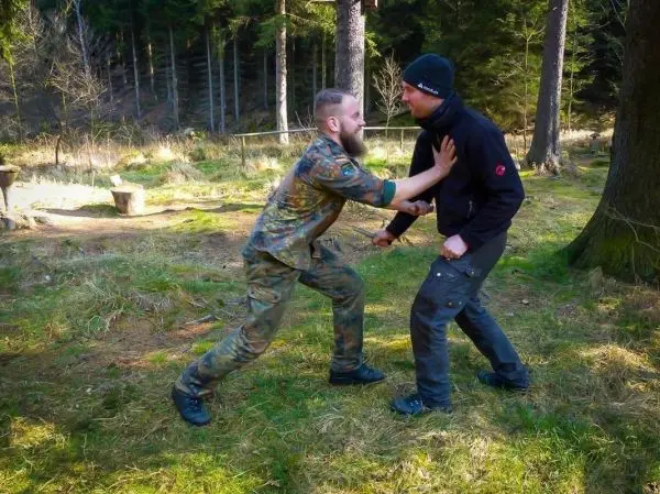 Zwei Personen üben eine Nahkampftechnik im Wald auf einer grünen Wiese