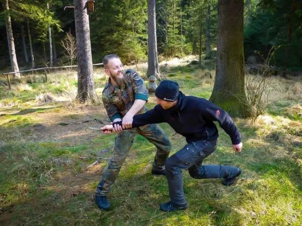 Zwei Personen üben eine Nahkampftechnik im Wald mit einem Stock
