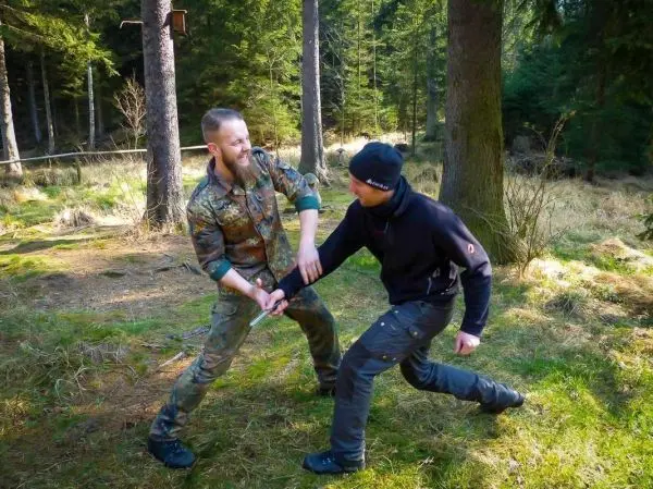 Zwei Personen üben einen Nahkampfgriff im Wald auf weichem Boden