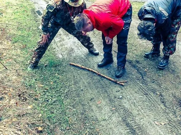 Drei Personen beugen sich über einen Stock auf einem Waldweg