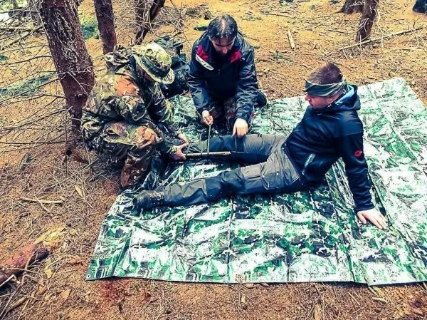 Drei Personen improvisieren eine Schiene zur Stabilisierung eines verletzten Beins