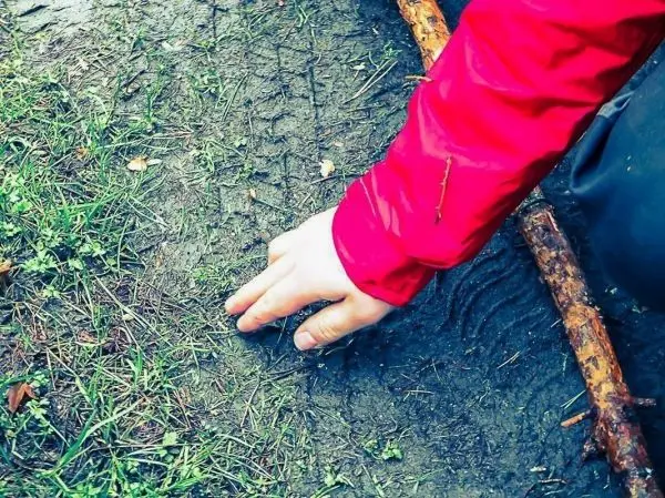 Hand berührt den Boden, während ein Stock daneben liegt