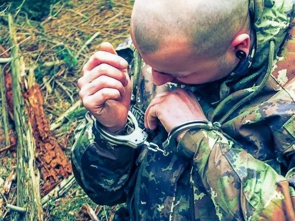Hand mit Handschellen an einem Kleidungsstück, Kopf leicht gesenkt