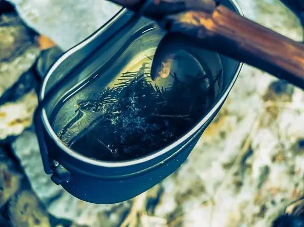 Kessel mit Wasser und Zweigen über Feuerstelle erhitzt