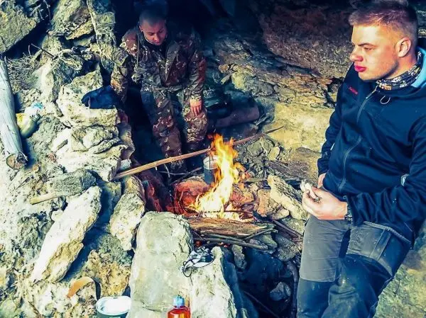 Kleine Flamme brennt zwischen Steinen, zwei Personen sitzen in einer Höhle