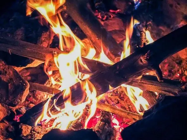 Kleine Flamme zwischen Holzstücken und Steinen, Glut sichtbar