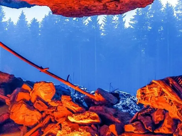 Kleines Bodenfeuer leuchtet in einer Höhle, umgeben von Steinen und Holz