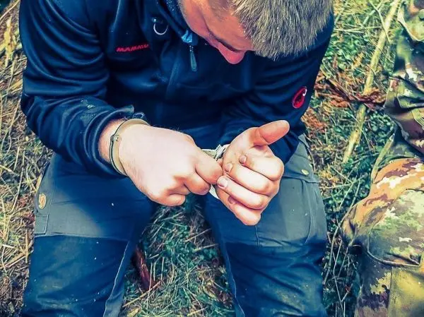 Mann löst Handschellen an seinem Handgelenk im Unterholz