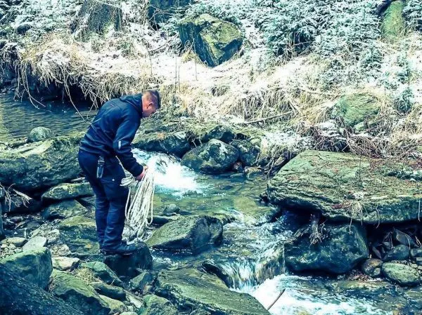 Mann steht auf einem Stein und hält ein Seil über einen kleinen Bach