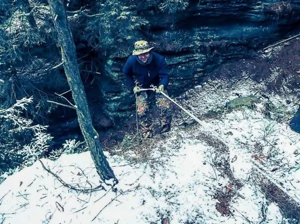 Mann zieht an einem Seil, um einen Hang zu erklimmen, umgeben von Schnee und Felsen