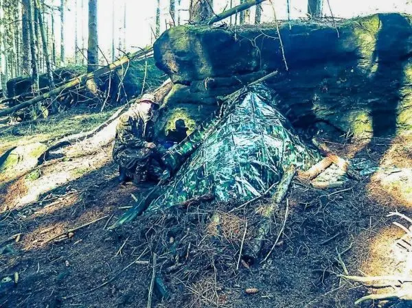 Person baut Tarp-Notunterkunft aus reflektierendem Material neben Felsen
