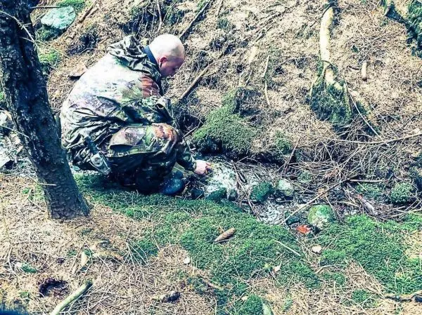 Person beugt sich über einen kleinen Bach im Wald