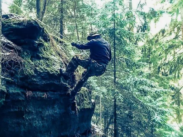 Person klettert mit Seil an einer Felswand im Wald