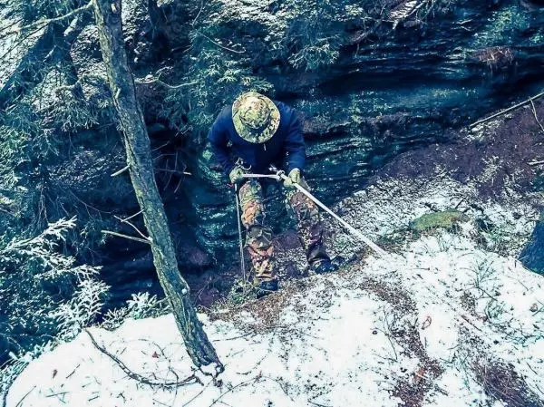 Person nutzt einen Stock zur Unterstützung beim Abseilen an einem steilen Hang