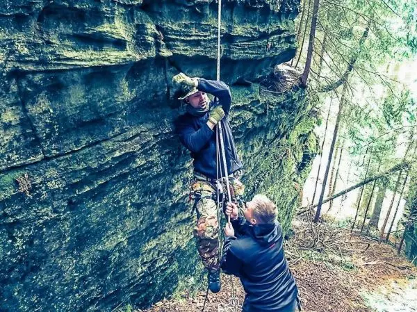 Person sichert andere Person beim Abseilen an Felswand