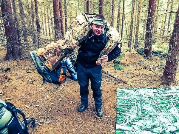 Person trägt eine große, gepolsterte Ausrüstung auf der Schulter im Wald