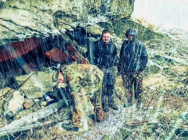 Person untersucht Feuerstelle unter Felsen, zwei Personen beobachten