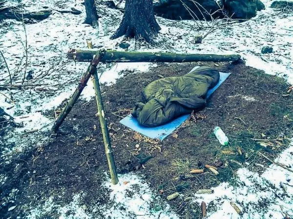 Tarp-Notunterkunft aus Ästen schützt Schlafsack auf dem Boden