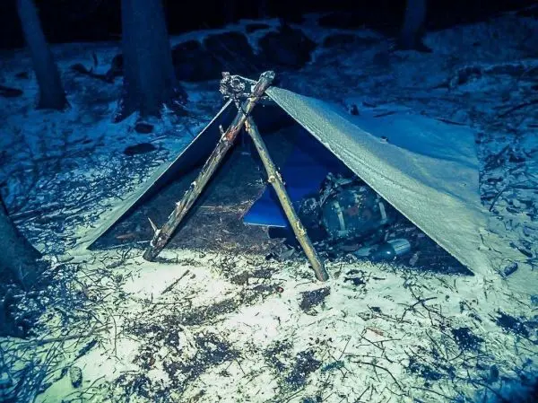 Tarp-Notunterkunft aus Ästen und Plane im Schnee aufgebaut