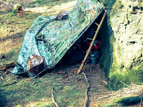 Tarp-Notunterkunft aus Folie und Ästen an einer Felswand