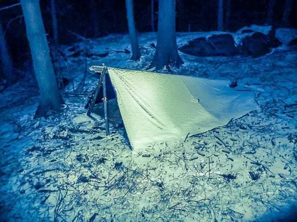 Tarp-Notunterkunft aus Plane und Holzgestell im Schnee zwischen Bäumen