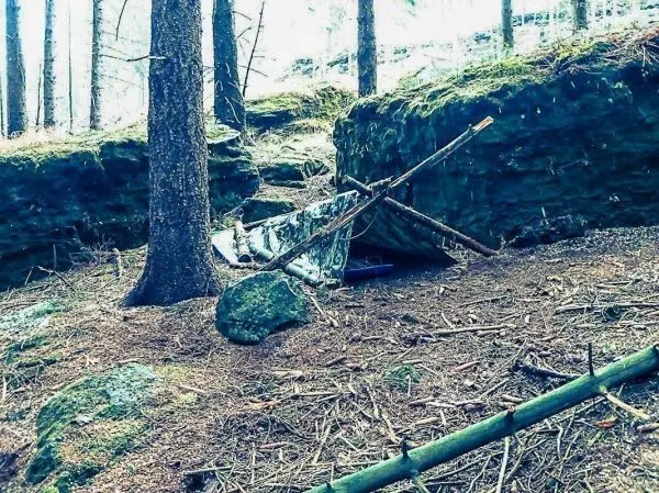 Tarp-Notunterkunft unter einem Felsen, gestützt von Ästen im Wald