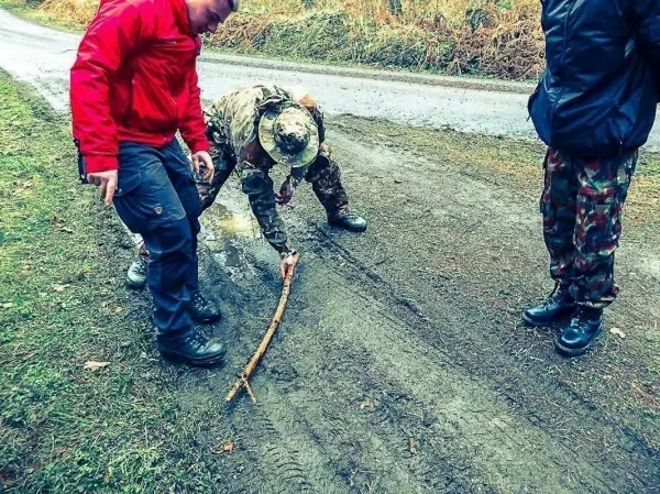 Zwei Personen beobachten, wie jemand mit einem Stock im Boden kratzt