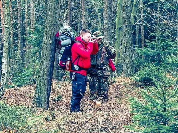 Zwei Personen im Wald, eine mit Rucksack beobachtet mit Fernglas