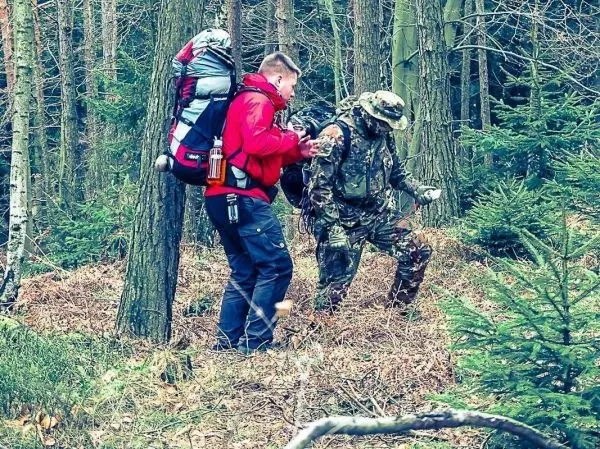 Zwei Personen im Wald helfen sich beim Überqueren von unebenem Gelände