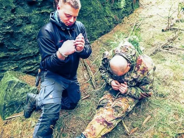 Zwei Personen knien im Wald, eine Person führt eine Handgelenk-Fesselung durch