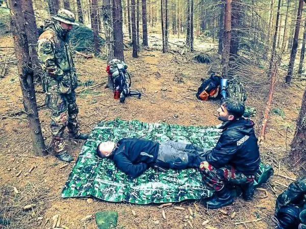 Zwei Personen leisten Erste Hilfe auf einer Plane, während eine dritte Person beobachtet