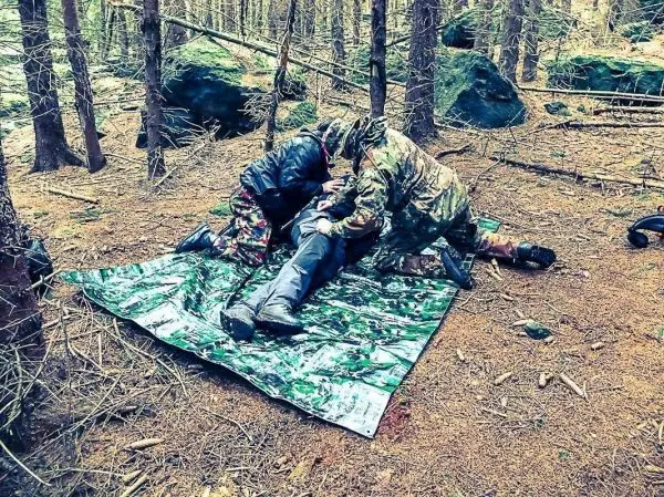 Zwei Personen leisten Erste Hilfe auf einer Tarp-Notunterkunft im Wald