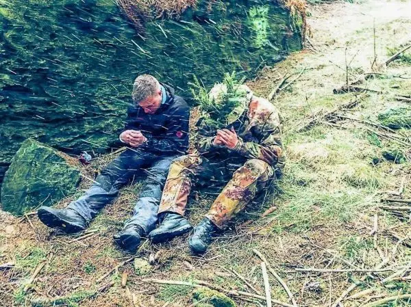 Zwei Personen sitzen auf dem Boden, umgeben von Wald und Steinen