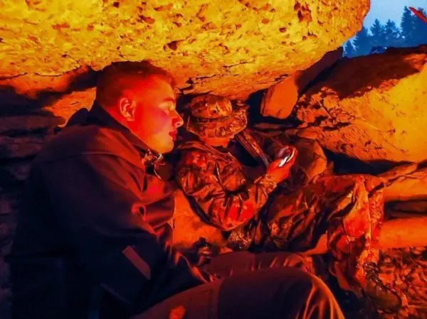 Zwei Personen sitzen unter einem Felsen und nutzen ein Handy