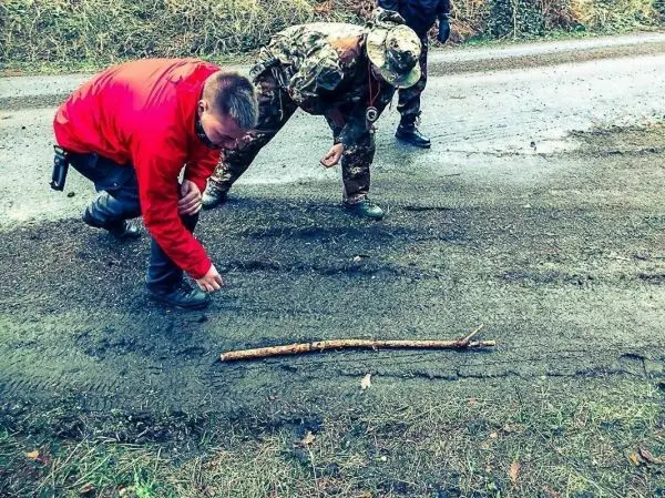 Zwei Personen untersuchen eine Spur im Boden neben einem Stock