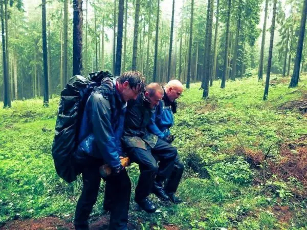 Drei Personen mit Rucksäcken beugen sich in einem Wald über den Boden